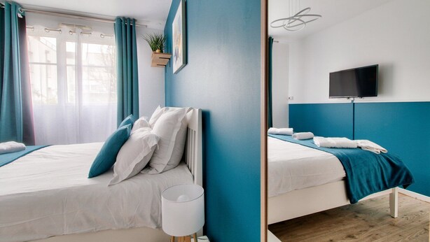 A modern hotel room with two beds, a flat-screen TV, and a window with curtains.