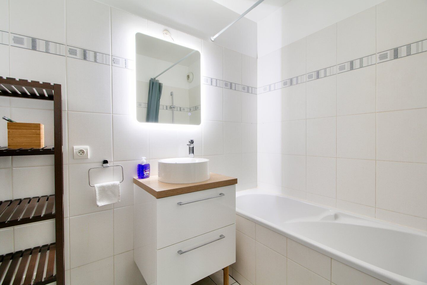 Un baño moderno con un lavamanos blanco, encimera de madera y una bañera grande.