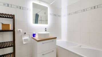 Un baño moderno con un lavamanos blanco, encimera de madera y una bañera grande.