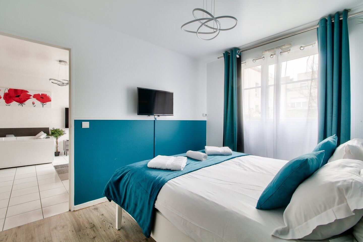 A modern hotel room with a bed, a TV, a bathroom, and a view of the city.
