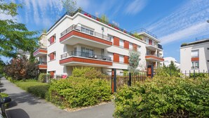 A multi-story residential building with balconies, a gated entrance, and surrounding greenery.