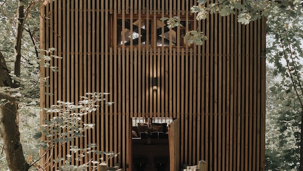 Una estructura de madera con listones verticales, una puerta central y un sendero de madera que la conduce.