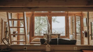 Interior acogedor de una cabaña con un banco de madera, una escalera y vistas al exterior a través de amplios ventanales.