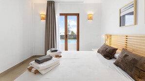 A modern hotel room with a large bed, a wooden headboard, a view of the outdoors through a glass door, and a painting on the wall.