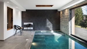 A modern indoor pool area with a stone wall and a clear view of the outdoors.