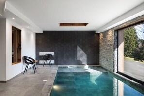 A modern indoor pool area with a stone wall and a clear view of the outdoors.