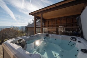 A hot tub with a wooden deck and a view of the mountains.