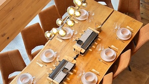 A long wooden dining table with multiple chairs, set with plates, glasses, and cutlery.