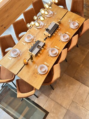A long wooden dining table with multiple chairs, set with plates, glasses, and cutlery.