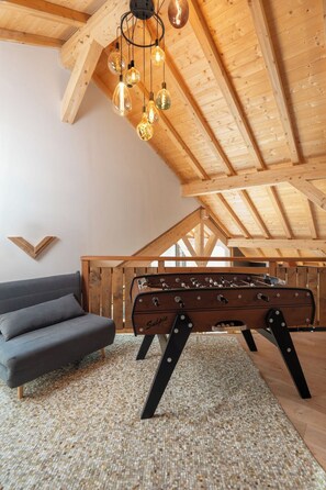 A loft-style room with a sofa, a foosball table, and a wooden ceiling with exposed beams.