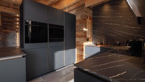 A modern kitchen with dark cabinetry, a built-in oven, and a marble countertop.