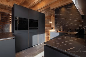A modern kitchen with dark cabinetry, a built-in oven, and a marble countertop.