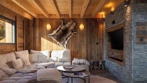 A cozy living room with a stone fireplace, wooden walls, and a leather hide mounted on the wall.