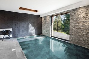 A modern indoor swimming pool with stone walls and a view of the outdoors.