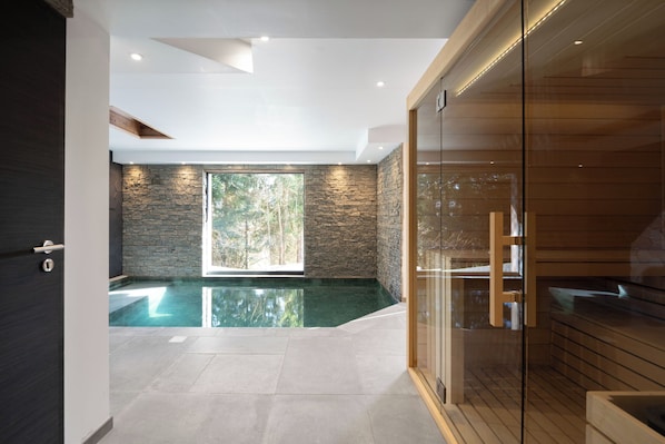 A modern interior with a stone wall, a glass-enclosed sauna, and a clear pool area.