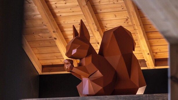 A geometric, abstract sculpture of a squirrel in a wooden interior space.