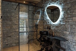 A bathroom with stone walls, a heart-shaped mirror, and a rustic wooden table.