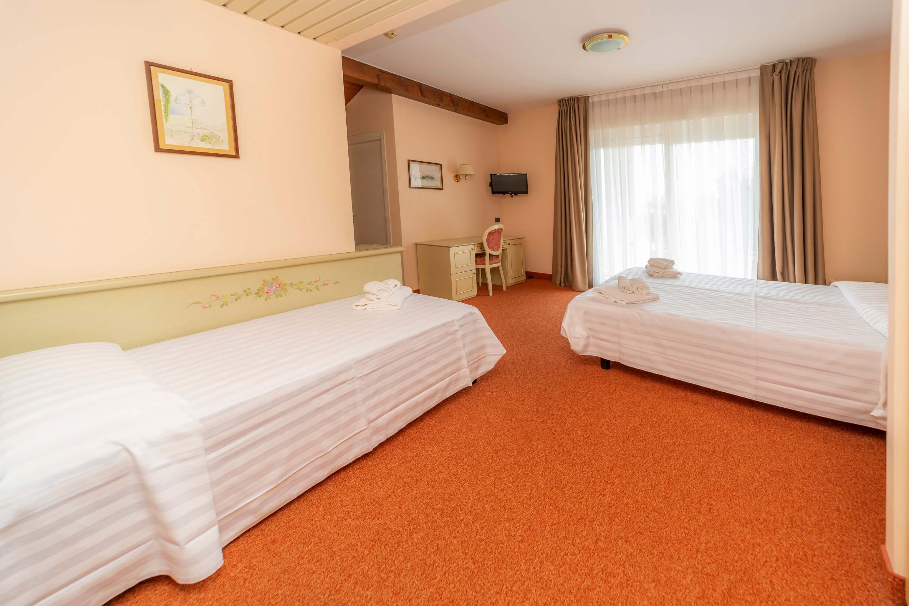 A hotel room with two single beds, a desk, a chair, a television, and a window with curtains.