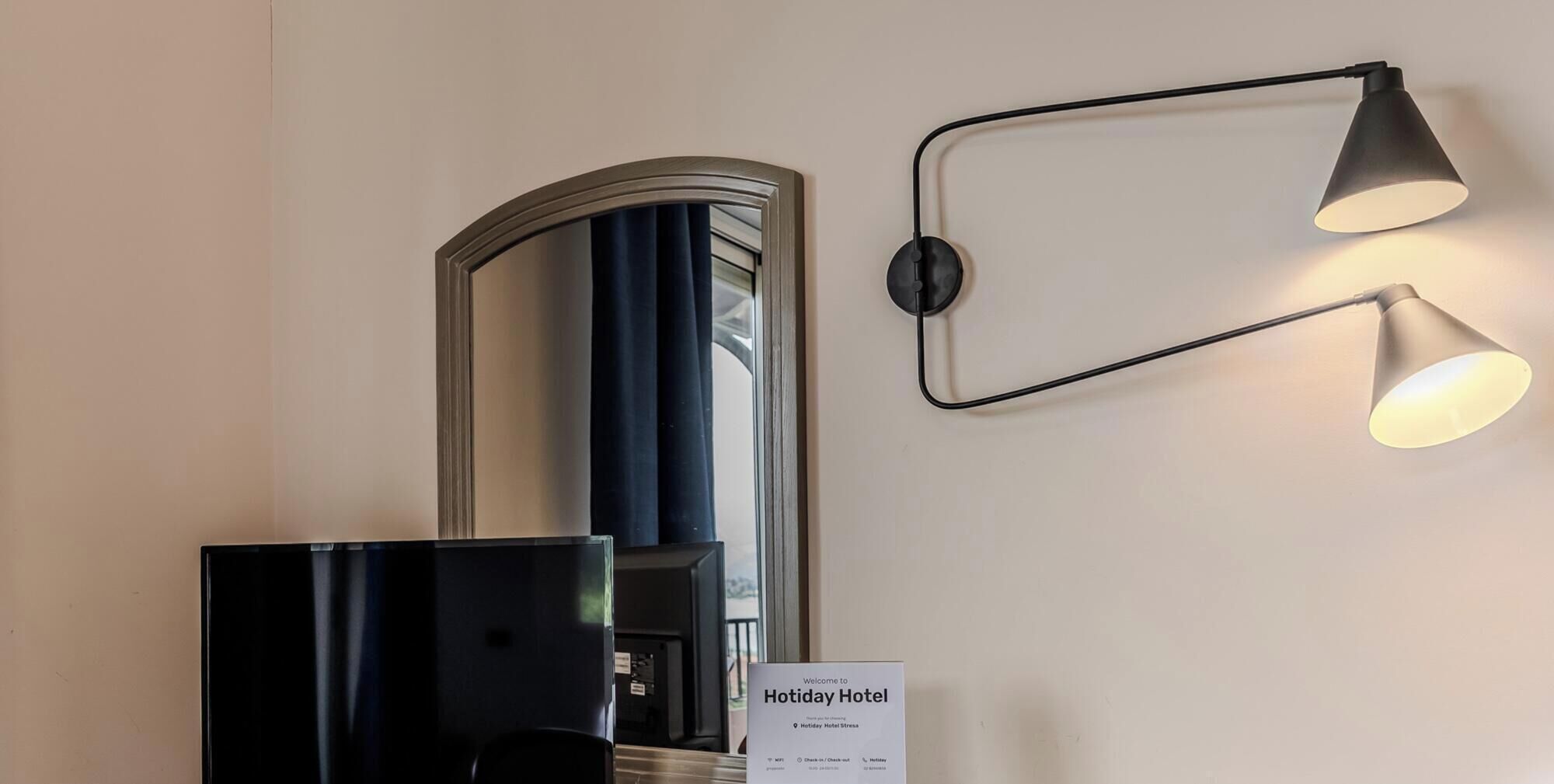 A reception desk with a sign indicating the Holiday Hotel, a wall-mounted mirror, and a modern wall lamp.