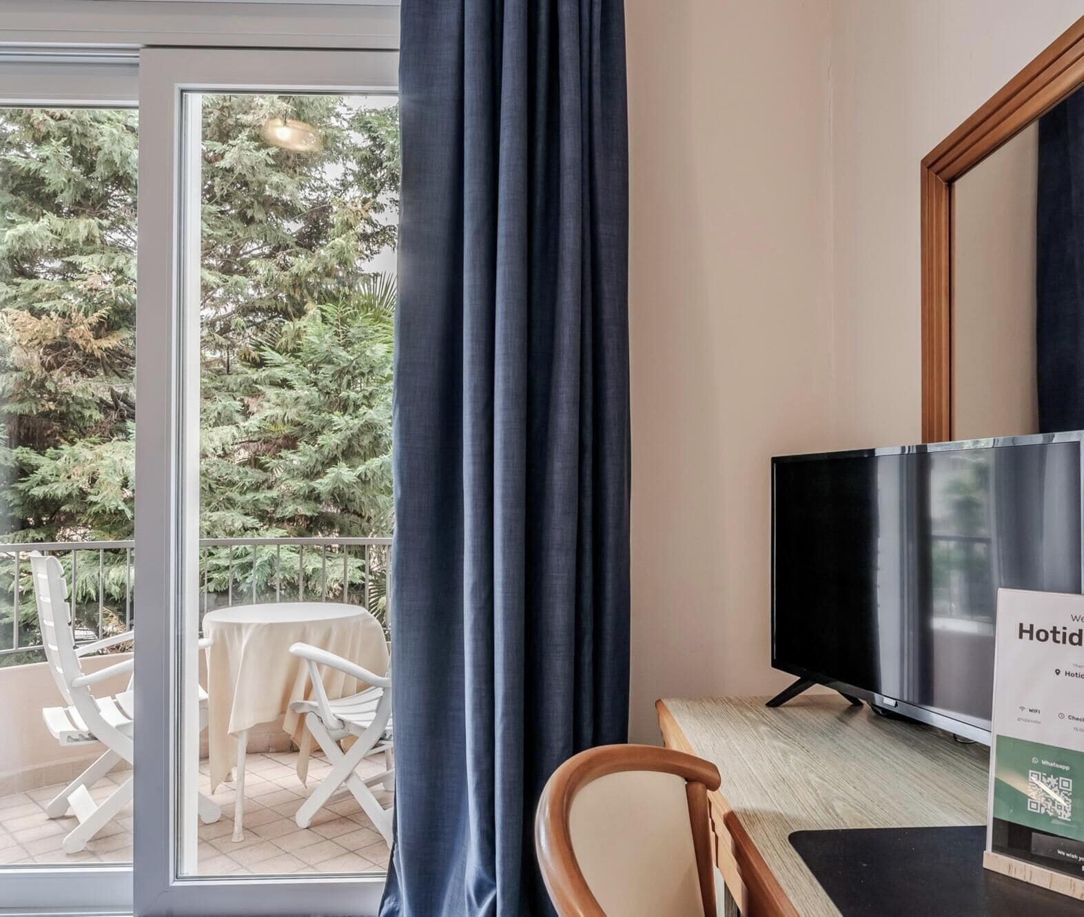 Una camera d'albergo con una grande finestra, una TV a schermo piatto, una sedia di legno e un tavolo.