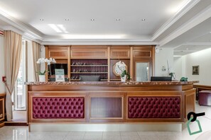 A reception area with a wooden reception desk, a clock, and a plant. - Hotiday Room Collection - Stresa (Stresa)