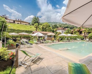 A pool area with lounge chairs and umbrellas, surrounded by greenery and buildings. - Hotiday Room Collection - Stresa (Stresa)