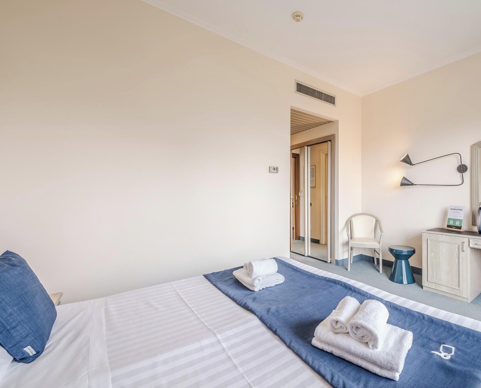 A hotel room with a bed, a chair, a desk, and a mirror.