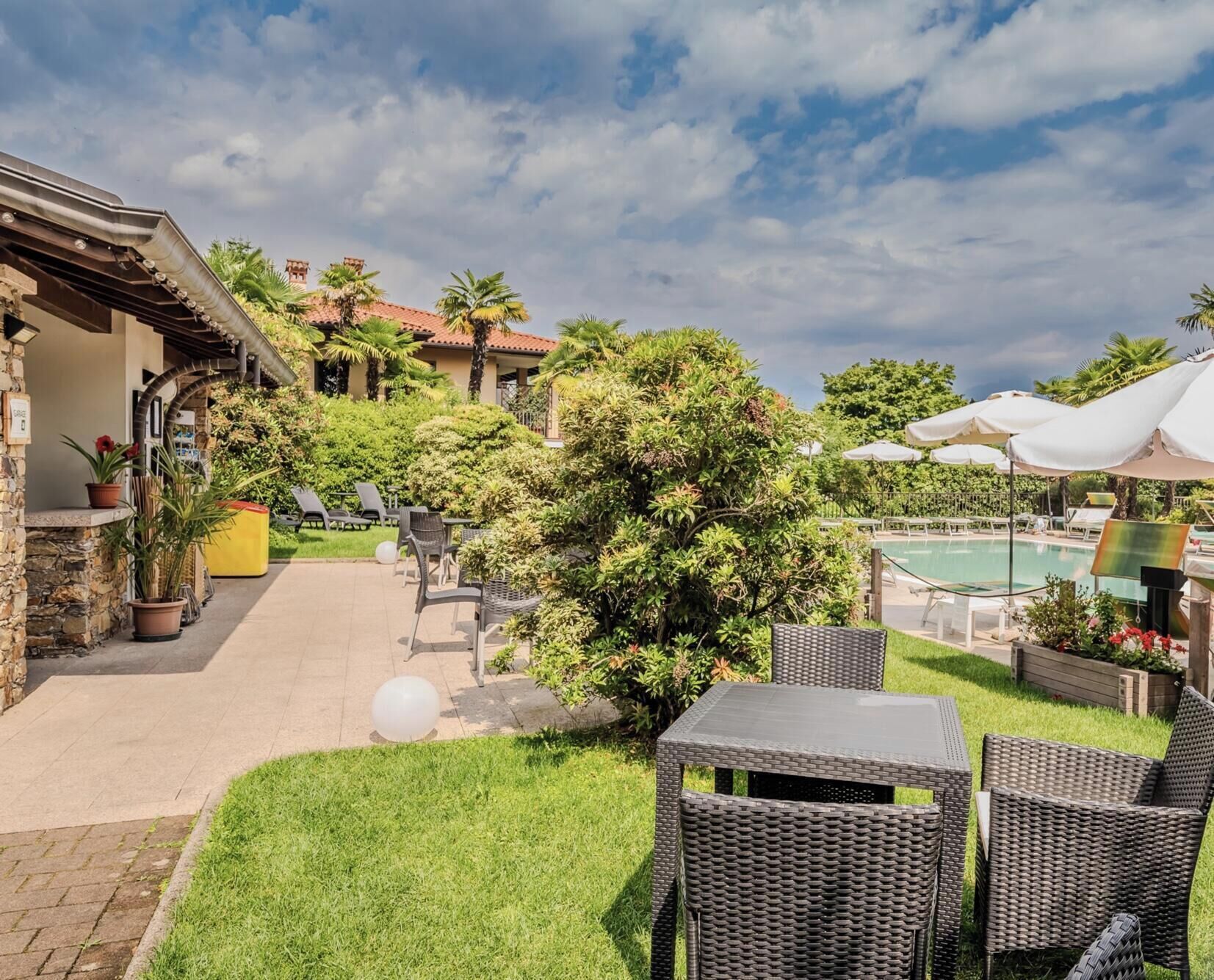 A patio area with wicker furniture, a pool, and lush greenery.