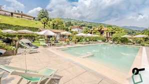 Un espace piscine doté de chaises longues et de parasols, entouré de verdure et de collines.