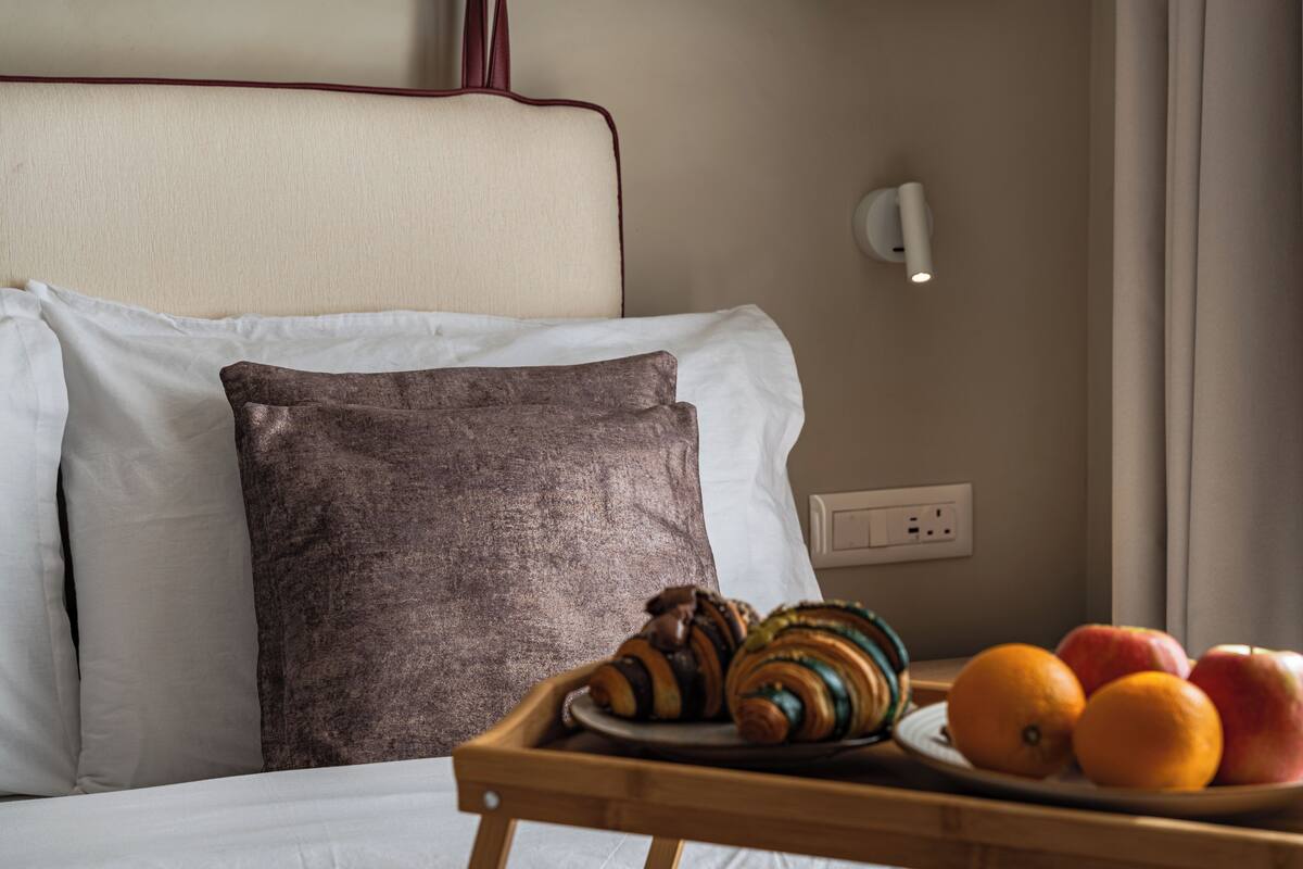 Una cama bien hecha con almohada y una bandeja de frutas y pasteles.