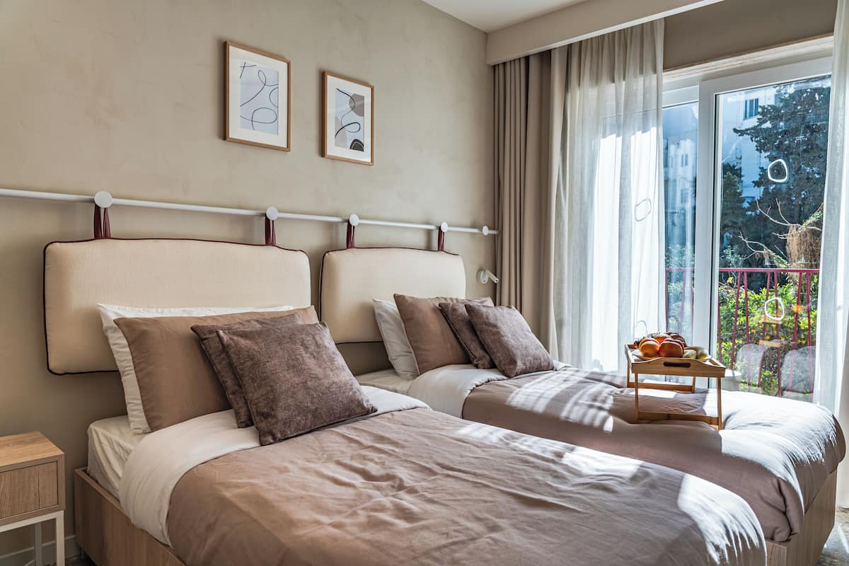 Habitación de hotel con dos camas, una mesita con fruta y un balcón con vistas a zonas verdes.