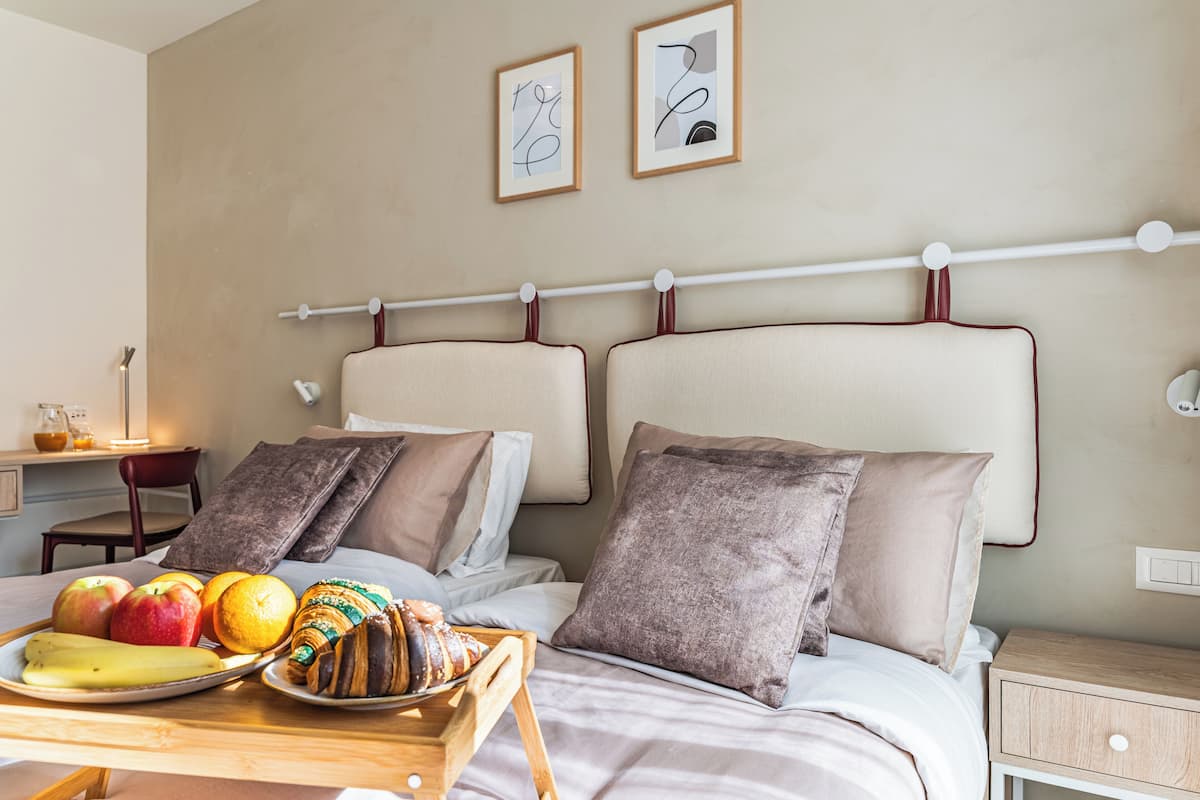 Habitación de hotel con dos camas, una mesita de noche con bandeja de desayuno y una obra de arte en la pared.