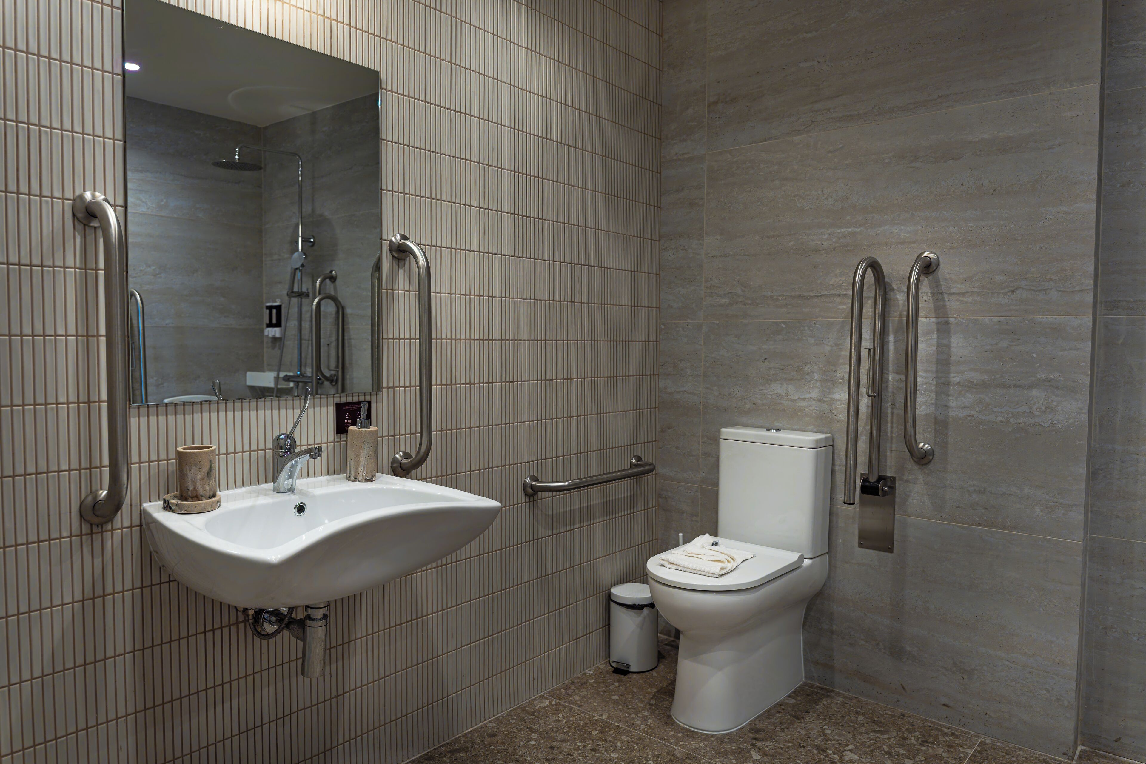 A modern bathroom with a sink, mirror, toilet, and grab bars.
