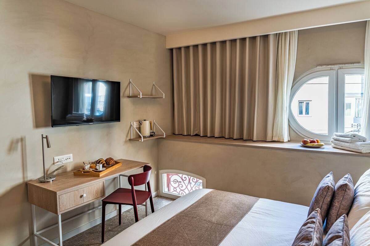 Habitación de hotel con cama, escritorio con silla, televisión y ventana con cortinas.