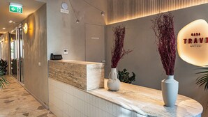 Een hotel receptie met een marmeren balie, een receptiemedewerker en twee vazen met gedroogde planten.