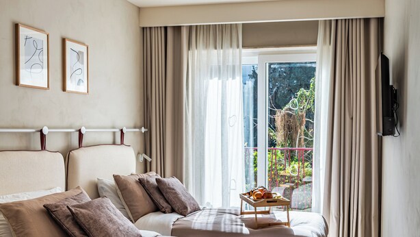 Een moderne hotelkamer met een groot bed, een tafeltje met fruit en een balkon met gordijnen.
