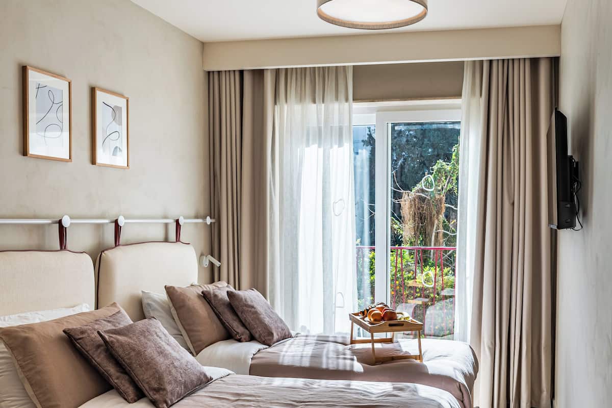 Habitación de hotel moderna con una cama grande, una mesita con fruta y un balcón con cortinas.