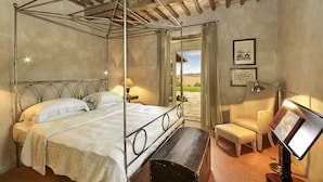 A four-poster bed with a wooden bench, a desk with a lamp, and a view of the outdoors. - AMORE RENTALS - Villa Valle with Pool, Garden, Ideal for Weddings (Sarteano)