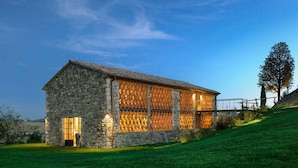 A stone building with large windows and a sloped roof, surrounded by a grassy area. - AMORE RENTALS - Villa Valle with Pool, Garden, Ideal for Weddings (Sarteano)