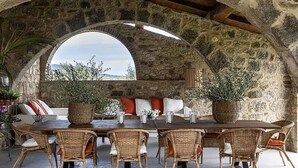 A stone-walled dining area with a high table and wicker chairs, overlooking a scenic landscape. - AMORE RENTALS - Villa Viola with Pool, Garden, Ideal for Weddings (Sarteano)