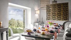 A dining area with a view of the outdoors, a table set with various dishes, and modern chairs. - AMORE RENTALS - Villa Viola with Pool, Garden, Ideal for Weddings (Sarteano)