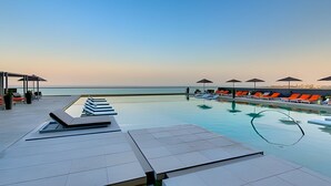 Un espace aménagé au bord de la piscine, avec des chaises longues et des parasols, offrant une vue sur une mer calme.