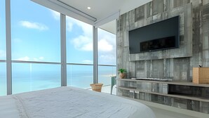 Une chambre avec un grand lit, un téléviseur fixé au mur et une vue sur l’océan.
