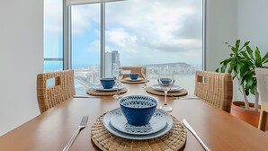 Une table à manger avec des bols et des assiettes à motifs bleus, ainsi que des couverts, dans une pièce dotée de grandes fenêtres donnant sur la ville.