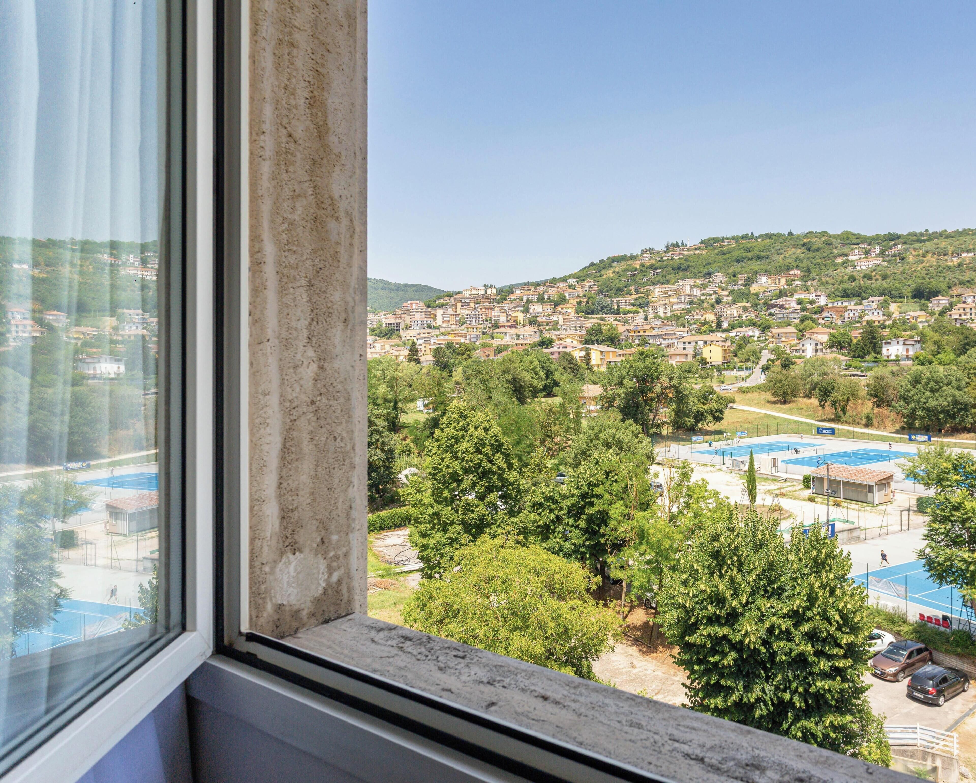 A view from a window overlooking a residential area with houses, trees, and a sports court.