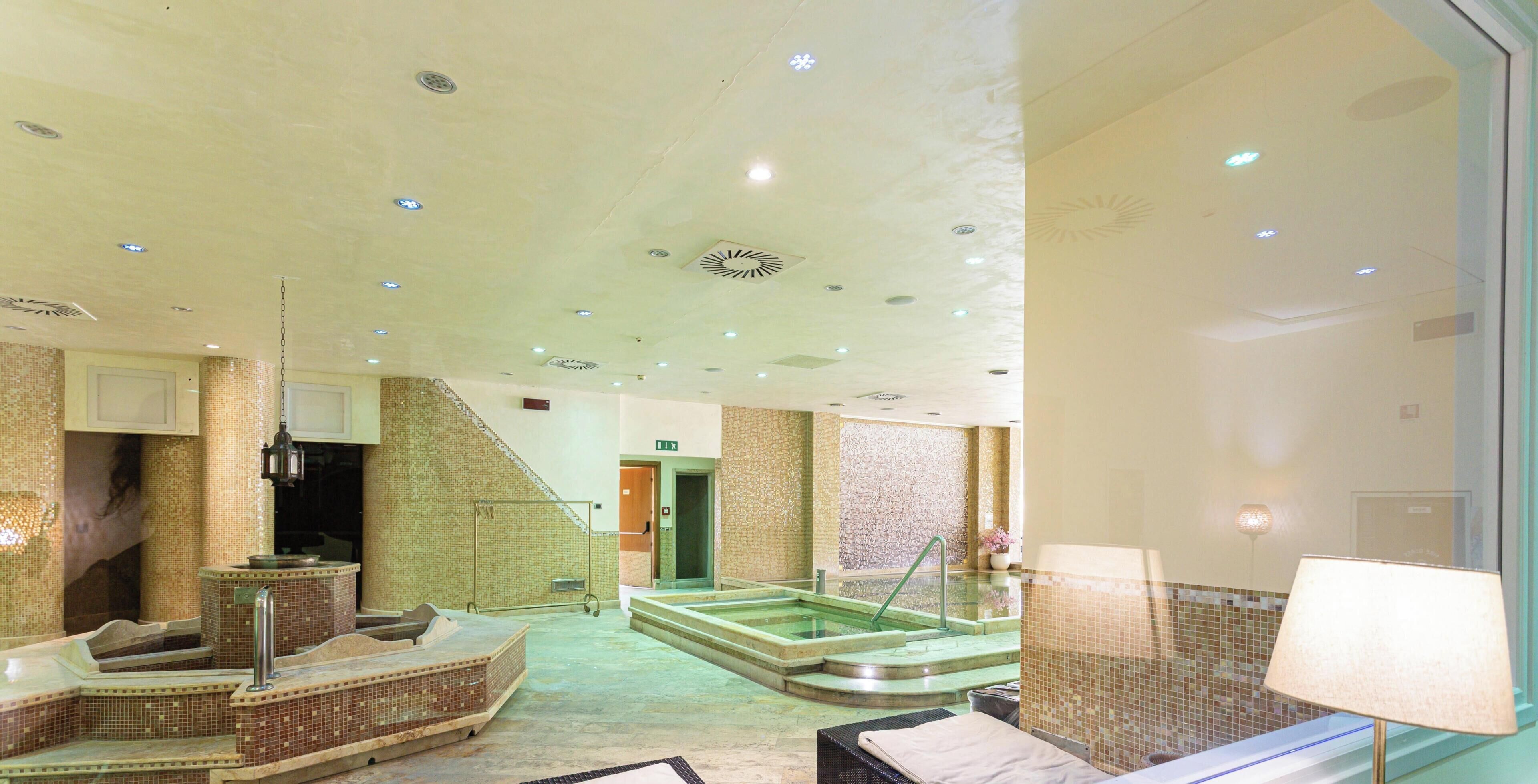 A hotel lobby with a reception desk, a seating area, a staircase, and a pool.
