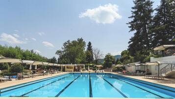 Una piscina con sillas de descanso y sombrillas, rodeada de árboles y un cielo despejado.