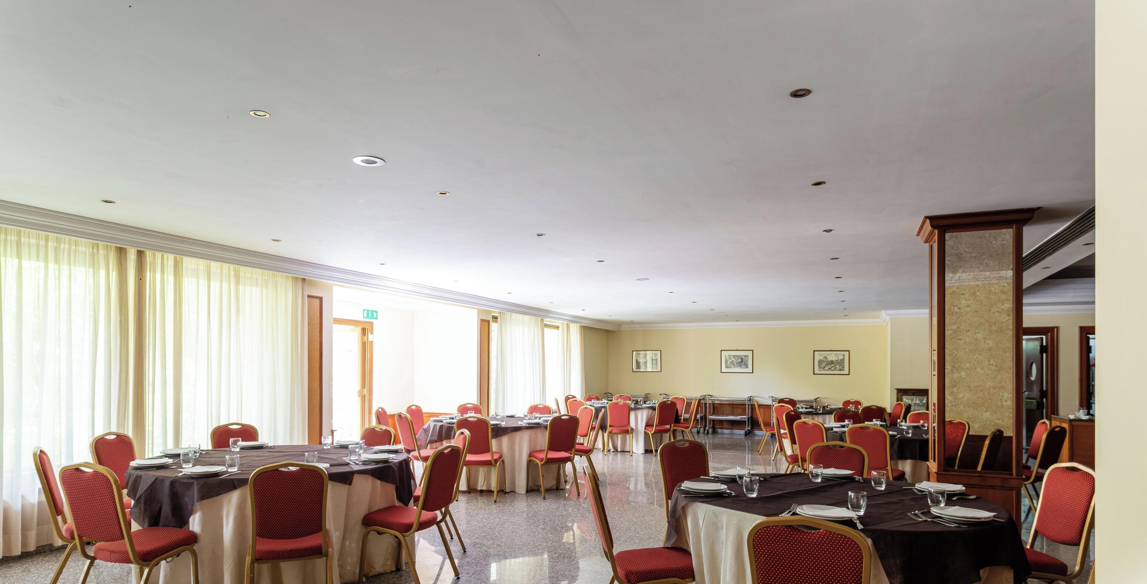 Una sala conferenze con diversi tavoli e sedie, ampie finestre con tende e un alto soffitto con illuminazione a incasso.