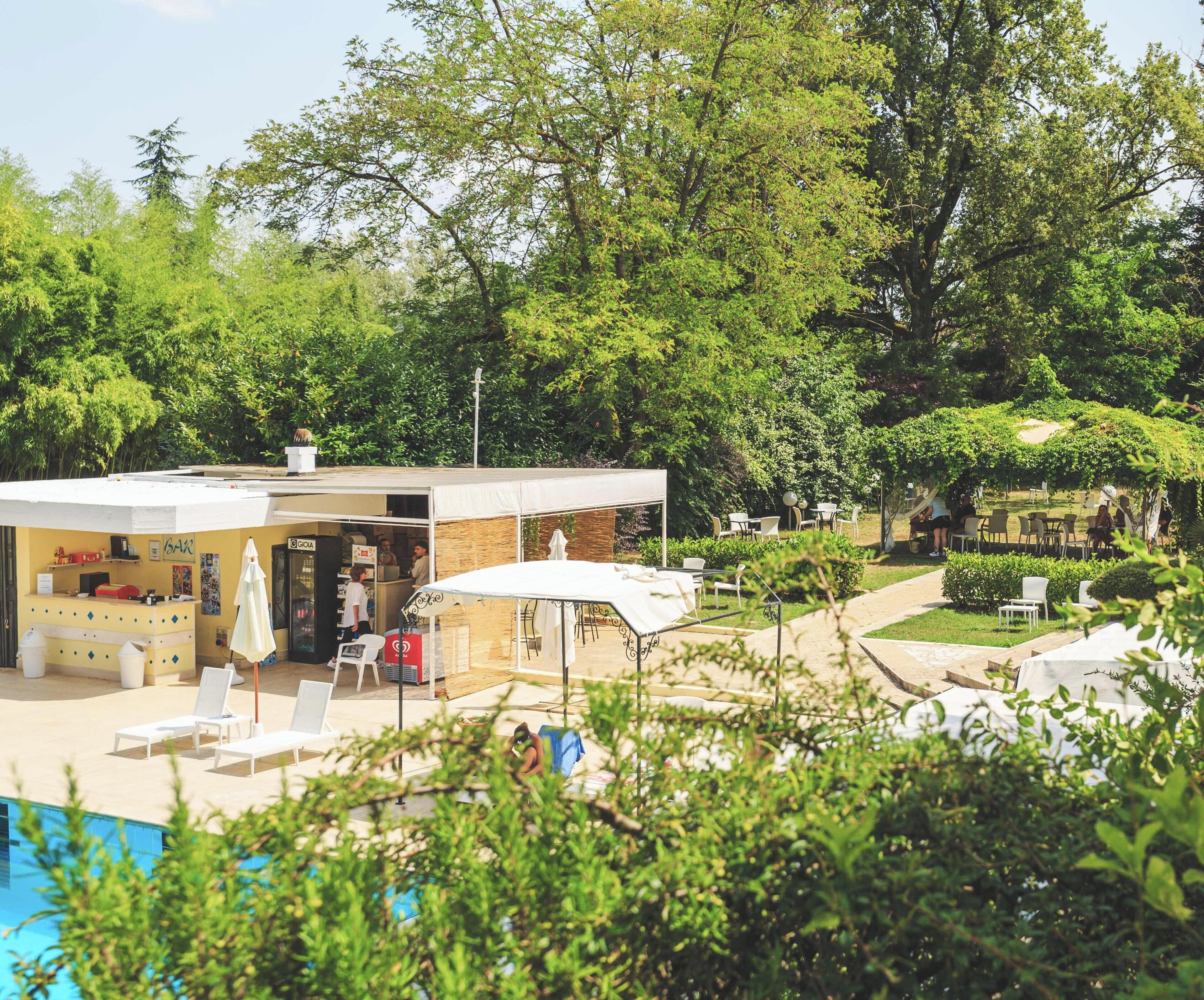 Zona junto a la piscina con bar, asientos al aire libre y un porche cubierto.
