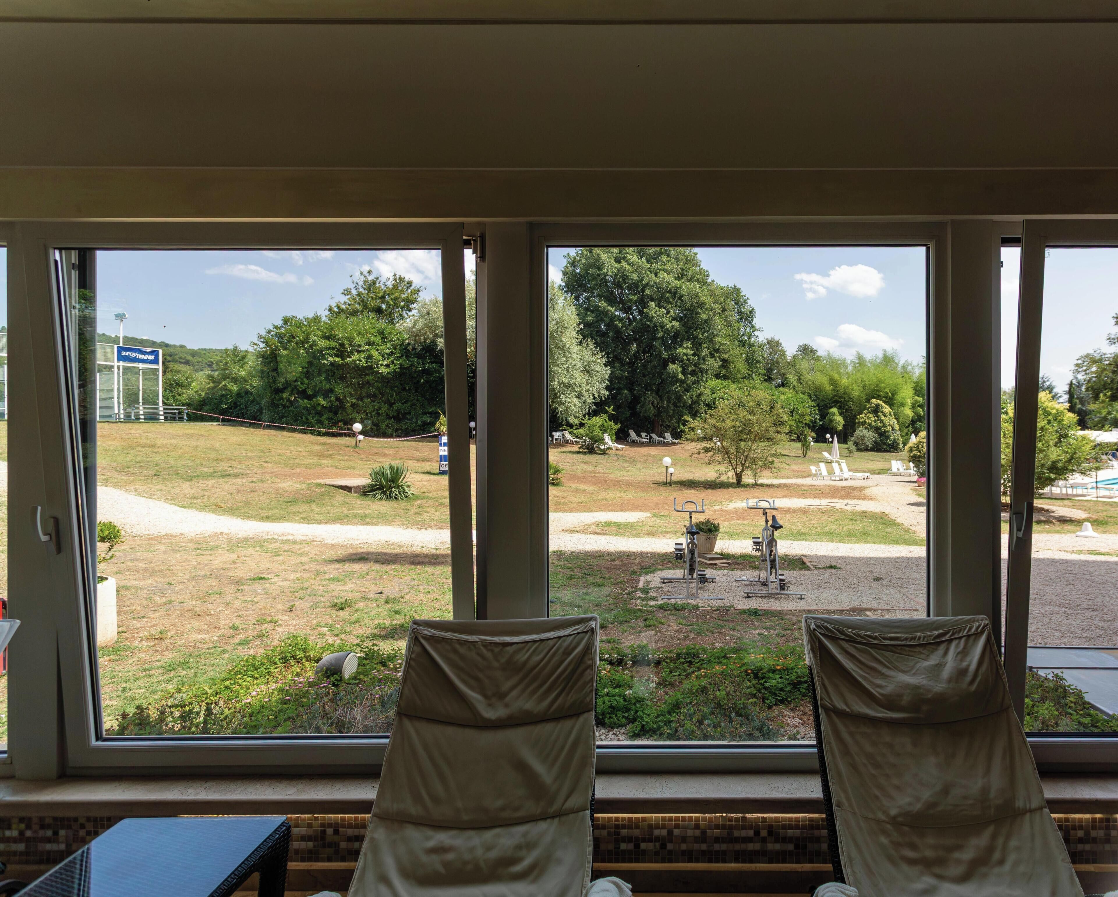 A room with a view of an outdoor area including a lawn, exercise equipment, and a sign for a nearby facility.